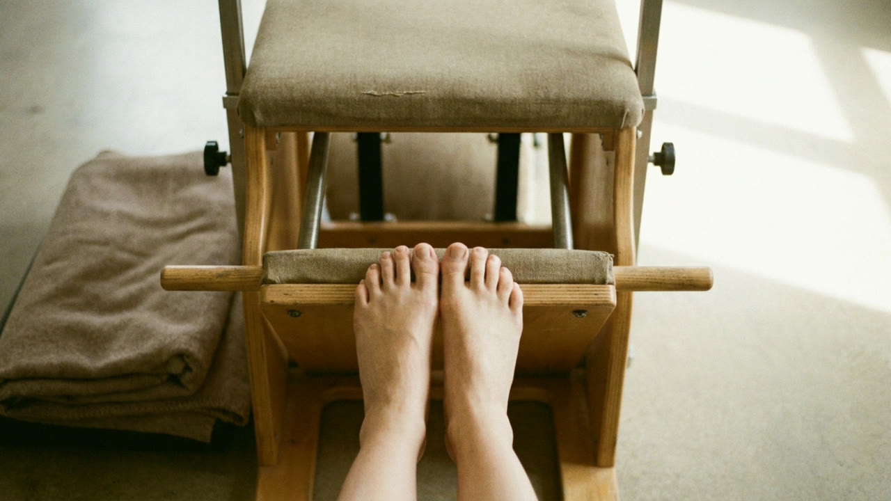 Bare feet aligned on a Pilates reformer footbar, seen from above