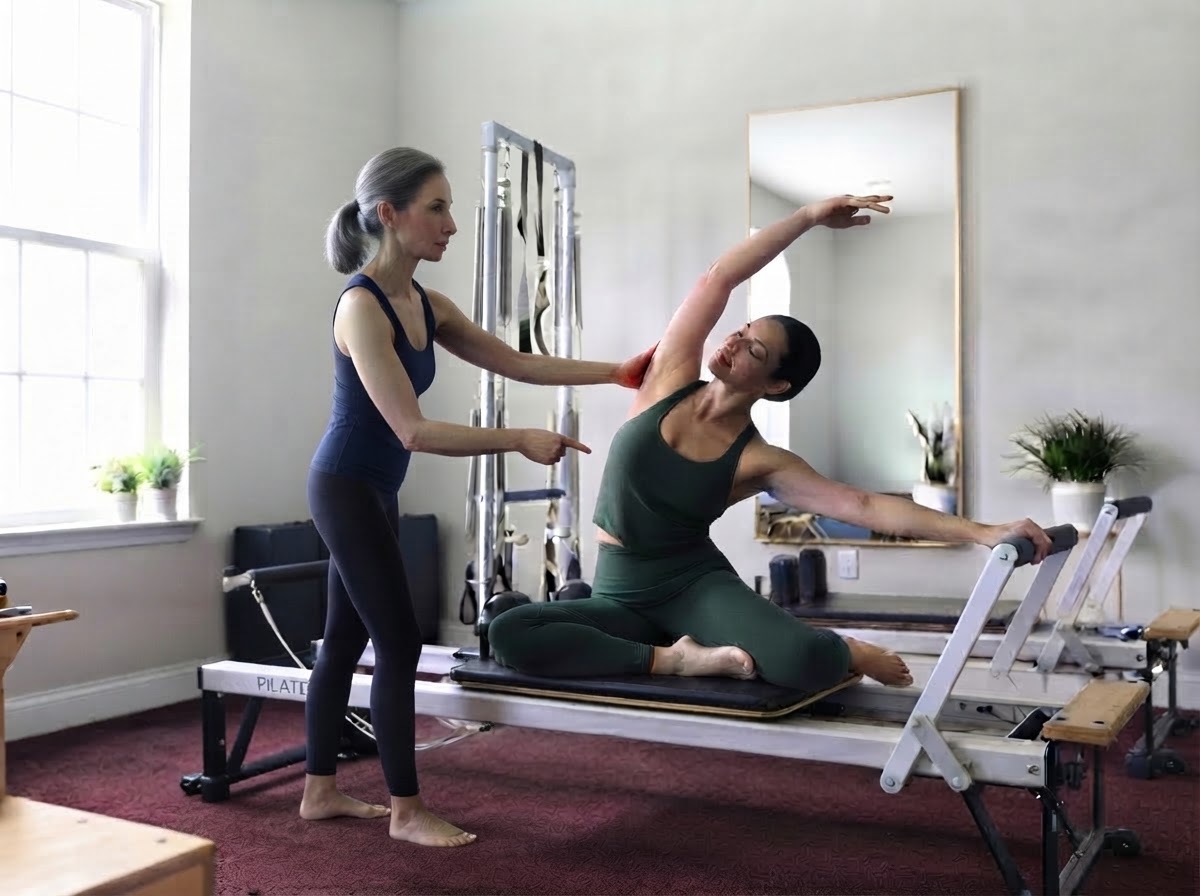 Gina Santangelo cueing a client through a seated side stretch on the Reformer at the GLOW Body studio