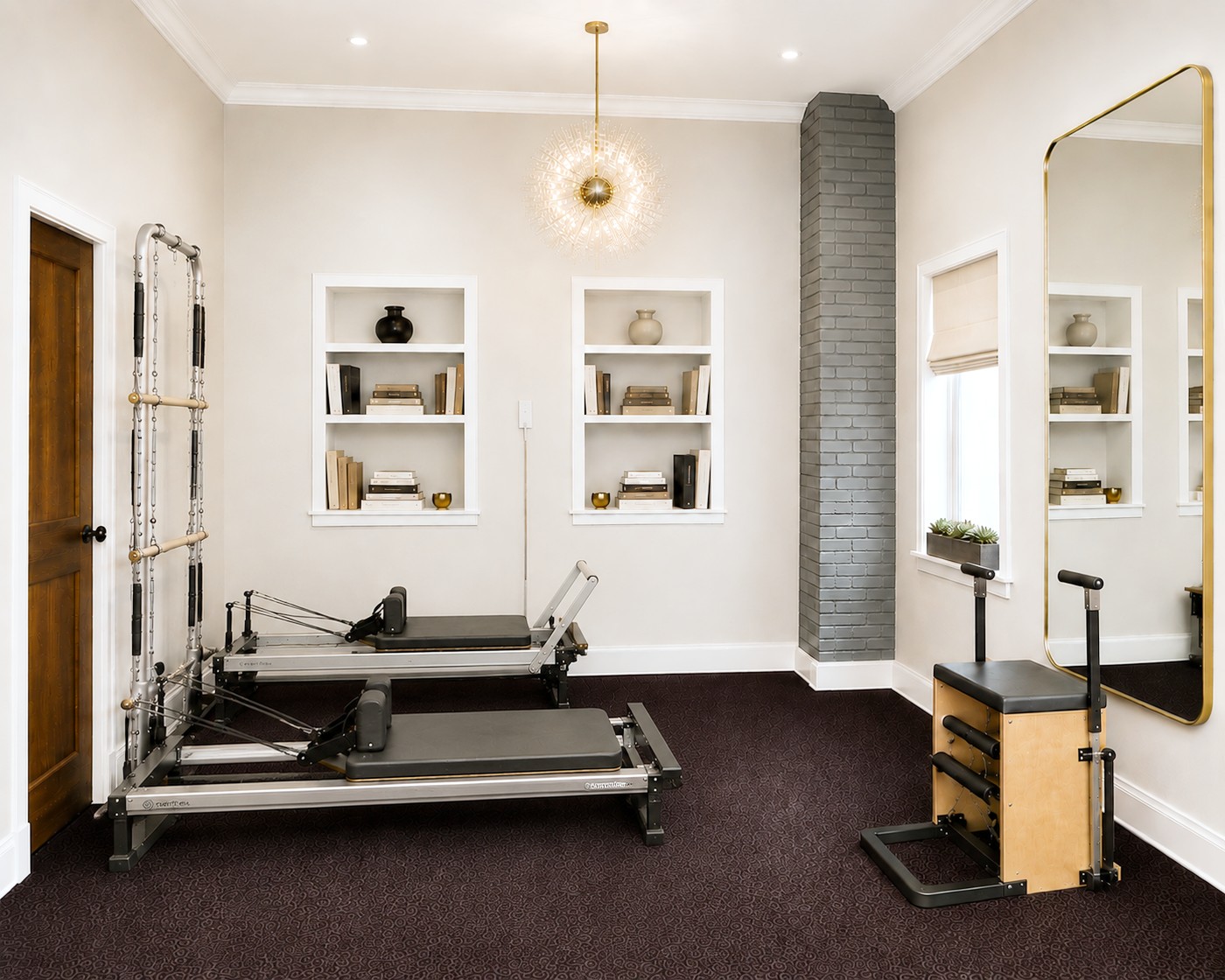 The GLOW Body Pilates studio in Ridgewood, NJ: two Merrithew reformers, a spine corrector and stability chair beneath twelve-foot ceilings, with built-in shelves and a gold-framed mirror