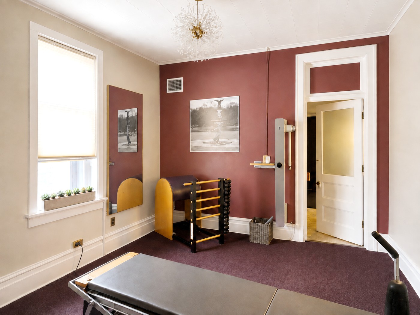 A second view of the GLOW Body studio: the ladder barrel and Cadillac tower against the oxblood wall, with the window and the original panelled door